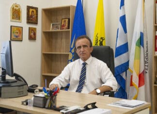 ΠΑΡΕΜΒΑΣΗ 02-01-2025 Ανδρας σε γραφείο με ελληνικές και ευρωπαϊκές σημαίες, συμβολίζει δημοκρατικές αξίες.