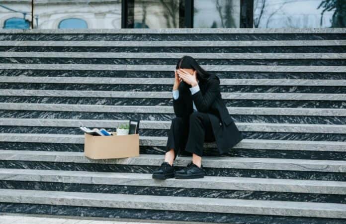 Ανεργία και κοινότητα. Άνεργη γυναίκα καθισμένη σε σκαλιά με κουτί αποκατοίκηση, συμβολισμός οικονομικής δυσκολίας.