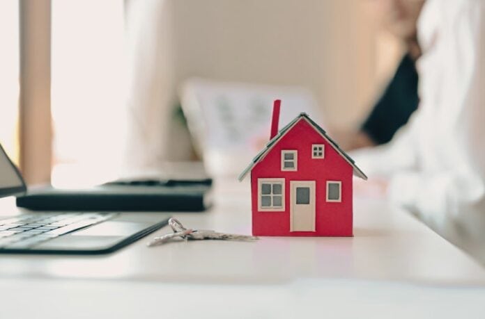 Οικογενειακό σπίτι μικρό μοντέλο σε γραφείο με κλειδιά, συμβολίζει την κατοικία και την ασφάλεια.