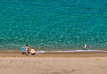 Στο σφυρί οι παραλίες μας: Η Κυβέρνηση μετατρέπει τον εθνικό μας πλούτο σε ψηφιακό εμπόρευμα! Παιδιά απολαμβάνουν το καλοκαίρι στην παραλία με σωσίβια και παιχνίδια.