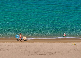 Στο σφυρί οι παραλίες μας: Η Κυβέρνηση μετατρέπει τον εθνικό μας πλούτο σε ψηφιακό εμπόρευμα! Παιδιά απολαμβάνουν το καλοκαίρι στην παραλία με σωσίβια και παιχνίδια.