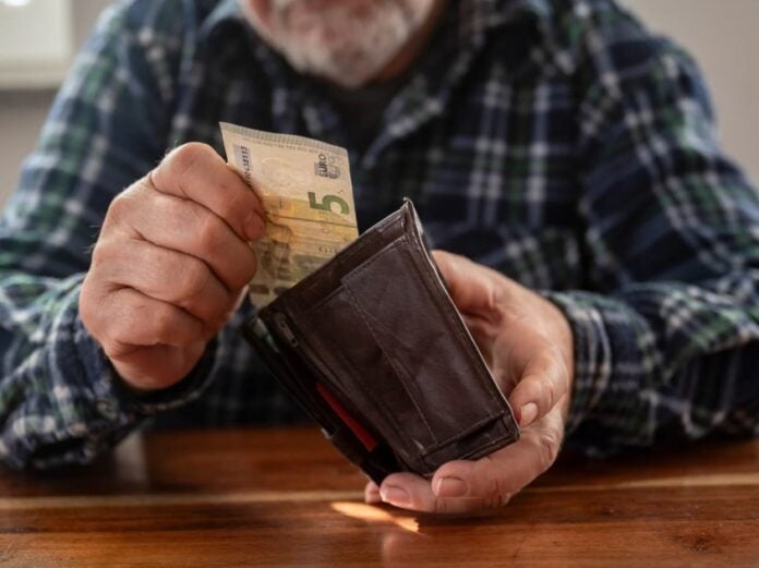 Άνθρωπος βάζει χρήματα σε πορτοφόλι, προωθώντας την οικονομική δικαιοσύνη.