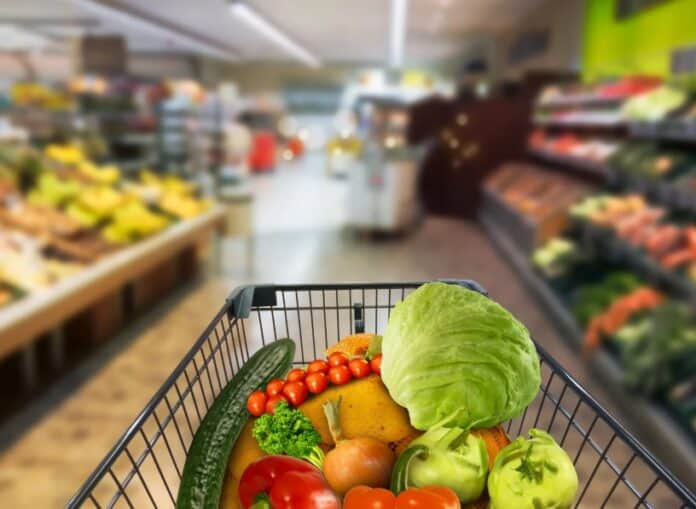 Ανθρώπινο καλάθι με φρέσκα φρούτα και λαχανικά σε σούπερ μάρκετ, ιδανικό για υγιεινή διατροφή.